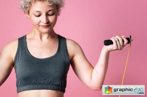 Young active girl with a skipping rope for cardio workout in a pink background studio